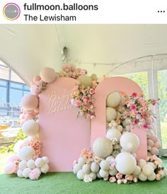 a pink and white balloon arch with balloons on the top, flowers in the bottom