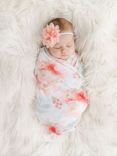 a newborn baby wrapped in a floral wrap on a white furnishing blanket with a pink flower pinned to it's head