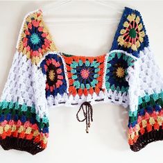 a colorful crocheted sweater hanging on a white wall next to a wooden hanger