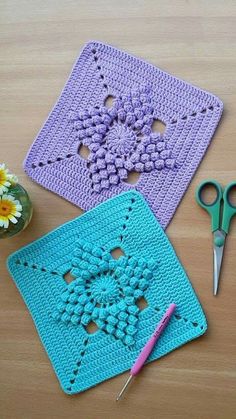 two crocheted coasters on a table with scissors and flowers in the background