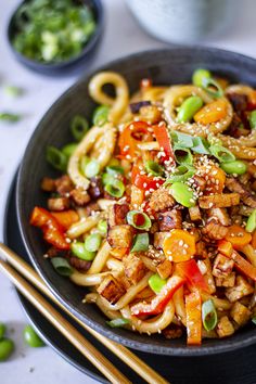 a black bowl filled with noodles and vegetables next to chopsticks on a table