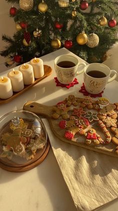 a table topped with cookies and cups of coffee next to a christmas tree filled with ornaments