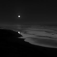 black and white photograph of the beach at night with full moon in sky over water