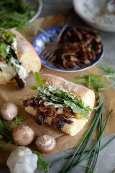 the sandwich is cut in half on the cutting board with mushrooms and herbs around it