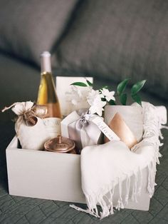 a bottle of wine sitting on top of a bed next to a white box filled with items