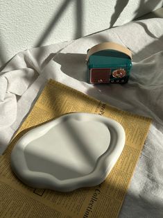 a white plate sitting on top of a bed next to a green radio and paper