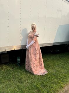 a woman standing next to a trailer in a pink dress and white gloves on her head