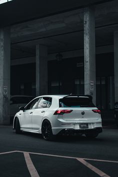 a white car is parked in an empty parking lot next to some concrete pillars and columns