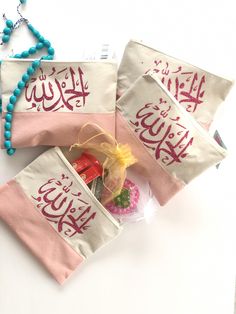 three small pouches with arabic writing on them and beaded necklaces next to each other