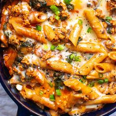 a blue skillet filled with pasta and meat covered in sauce, cheese and green onions