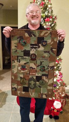 an older man holding up a quilt in front of a christmas tree with decorations on it