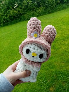 a hand holding a small stuffed animal in a crocheted hat and scarf on top of green grass