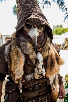 a man dressed up as a bird with a hood and feathers on his head, holding a dead animal in his hand