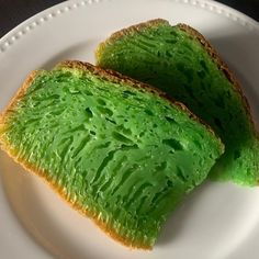 two pieces of bread with green icing on them sitting on a white plate next to each other