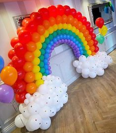 there is a rainbow balloon arch in the room with balloons all around it and on the floor