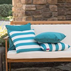 two blue and white pillows sitting on top of a bench next to a brick wall