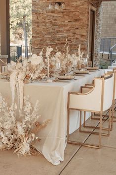 the table is set with white flowers and gold place settings for an elegant dinner party