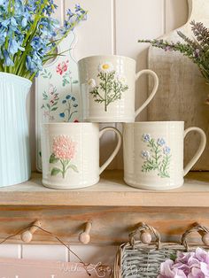 four mugs with flowers painted on them are sitting on a shelf next to a basket