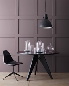 a dining table with two chairs and some glass vases on the table in front of a purple wall