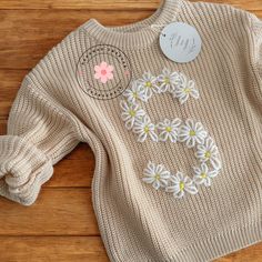 a knitted sweater with flowers on it and a name tag attached to the front