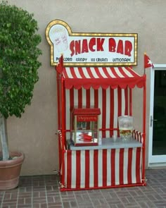 a red and white striped stand next to a potted plant on the side of a building