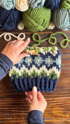 someone is knitting something with yarn and scissors on a wooden table next to some balls of yarn