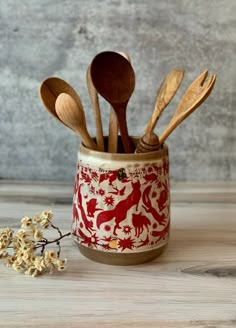 wooden spoons and utensils are in a red patterned cup with white flowers