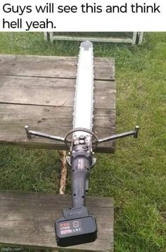 a chainsaw sitting on top of a wooden bench next to a grass covered field