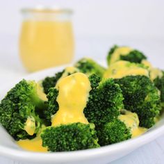 broccoli florets with cheese sauce in a white bowl next to a glass of orange juice