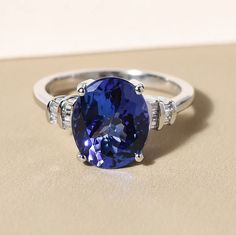 a tan and white gold ring with an oval blue sapphire surrounded by three round diamonds