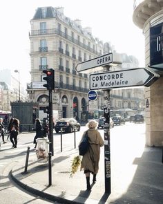 a woman walking down a street next to a traffic light with several signs on it