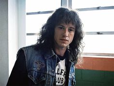 a man with long hair wearing a denim jacket and looking off to the side in front of a window