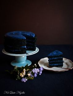 a piece of blue cake sitting on top of a white plate next to a flower