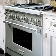 a silver stove top oven sitting inside of a kitchen next to white cabinets and drawers