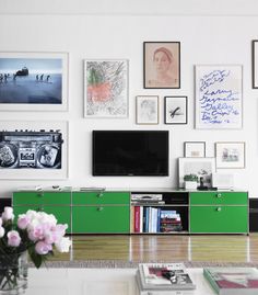 a living room with pictures on the wall and a television in the center, surrounded by flowers