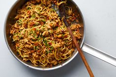 a skillet filled with noodles and meat on top of a table next to a wooden spoon