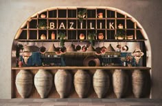 a shelf with vases and plants on it in front of a wall that says baziliki