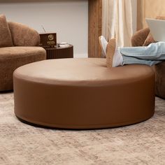 a person sitting on a round ottoman using a laptop computer in a living room area