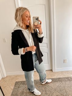 a woman taking a selfie in front of a mirror with her cell phone and wearing white sneakers