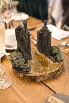 a wooden table topped with two figurines sitting on top of rocks next to wine glasses