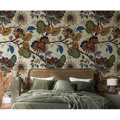 a bed sitting in front of a wall covered in colorful flowers and leaves on top of a wooden headboard