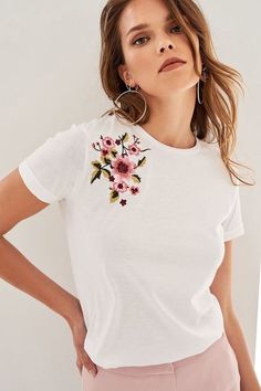 a woman in white shirt and pink pants with flower embroidered on the back of her t - shirt