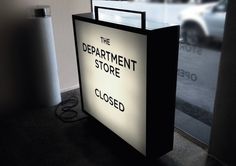 the department store closed sign is lit up in front of an open door with a car behind it