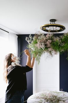 a woman arranging flowers on top of a table in a room with dark blue walls