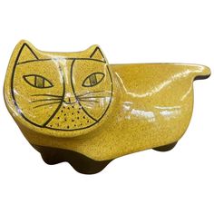 a yellow ceramic cat shaped dish with eyes on it's head, sitting in front of a white background