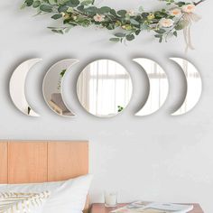 four circular mirrors mounted on the wall above a bed with flowers and greenery hanging from it