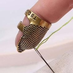 a hand holding a gold cuff with the word love on it and thread in front of it