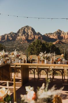 an outdoor dining table set up with flowers and greenery in front of the mountains