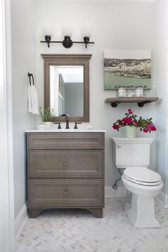 a white toilet sitting next to a wooden sink vanity in a bathroom under a mirror