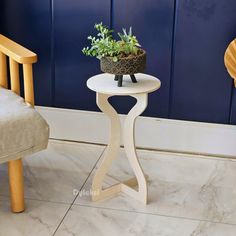 a small white table with a potted plant on it next to a chair in front of a blue wall